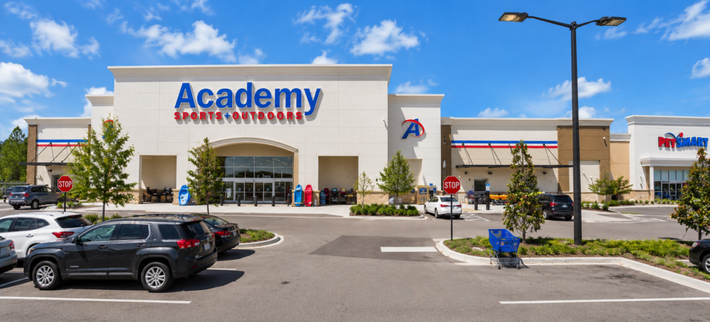 Imagem ilustrativa da Academy Sports + Outdoors no The Crosslands, em Kissimmee, com fachada da loja, estacionamento e PetSmart ao lado.